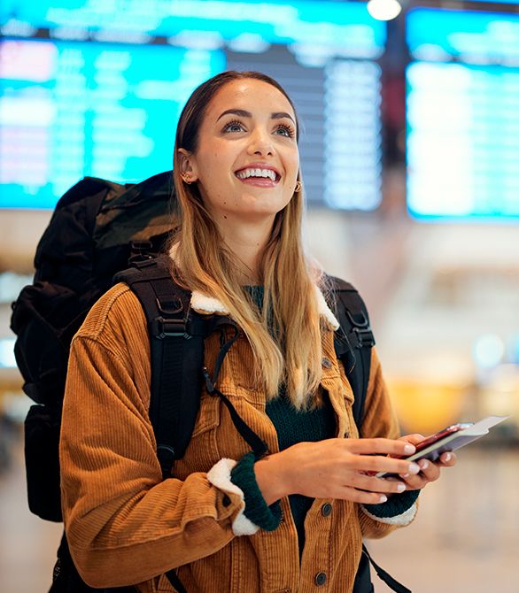 En ung kvinde står med en rygsæk på ryggen i en lufthavn og smiler.